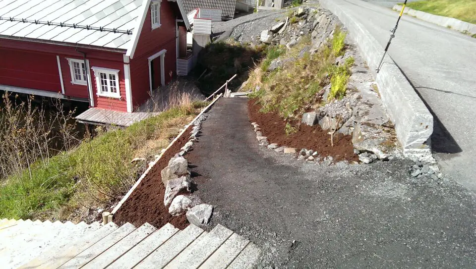 Ny gangsti med steinkant og bed ved et rødt hus